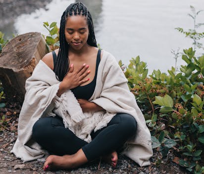 A woman practicing mindful meditation outdoors by the water, symbolizing wellness and relaxation.